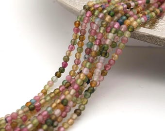 May include: A collection of small, round, translucent beads strung together in multiple strands. The beads feature a variegated color palette including shades of pink, olive green, yellow, and light blue, creating a multi-colored appearance.