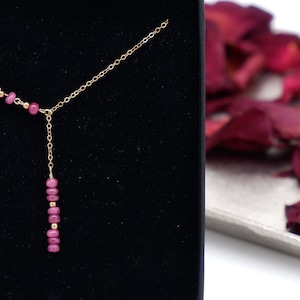 Könnte beinhalten: Eine goldene Kettenkette mit einem Anhänger aus rosafarbenem Edelstein. Der Anhänger besteht aus einer Reihe kleiner rosafarbener Edelsteine.