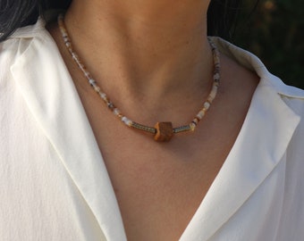Può includere: Una collana delicata realizzata con piccole perline multicolori e un ciondolo in legno a forma di cubo.