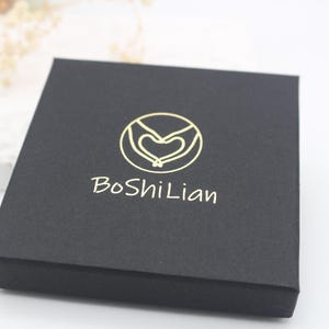 May include: A black box with a gold logo featuring two hands holding a heart. The text "BoShiLian" is printed in gold below the logo.