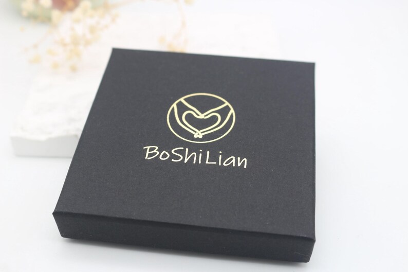 May include: A black box with a gold logo featuring two hands holding a heart. The text "BoShiLian" is printed in gold below the logo.