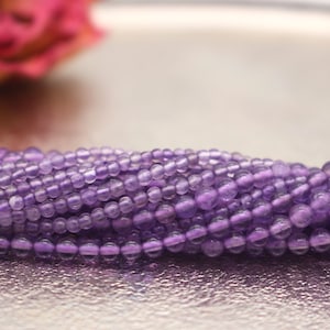 Könnte beinhalten: Eine Strähne kleiner, runder, violetter Amethystperlen. Die Perlen sind glatt und haben einen leichten Glanz.