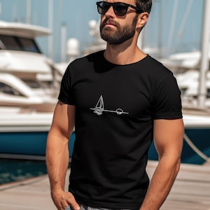 Peut inclure: Un t-shirt noir avec un dessin au trait blanc d'un voilier et d'un soleil couchant sur l'eau.