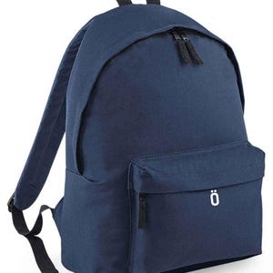 May include: A navy blue backpack with a front pocket and a top handle. The backpack features black zippers and straps. A white letter "ö" is printed on the front pocket.