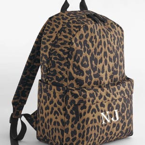 Peut inclure: Sac à dos à imprimé léopard marron et noir, avec une poignée supérieure, des bretelles réglables et une poche avant. Les initiales "NJ" dorées ornent la poche. Il possède un compartiment principal zippé et un panneau dorsal rembourré.