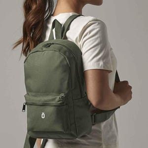 May include: Olive green backpack with a front zippered pocket and a top zipper closure. The backpack has adjustable straps and a small white logo on the front pocket. The backpack is made of a durable material and is designed for everyday use.