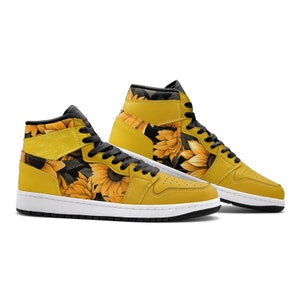 Puede incluir: Un par de zapatillas deportivas de caña alta amarillas con estampado de girasol. Las zapatillas tienen cordones negros y una suela blanca.