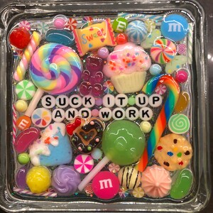 May include: A square glass box filled with colorful candy, sprinkles, and other sweet treats. The box has the words "SUCK IT UP AND WORK" spelled out in black letters.