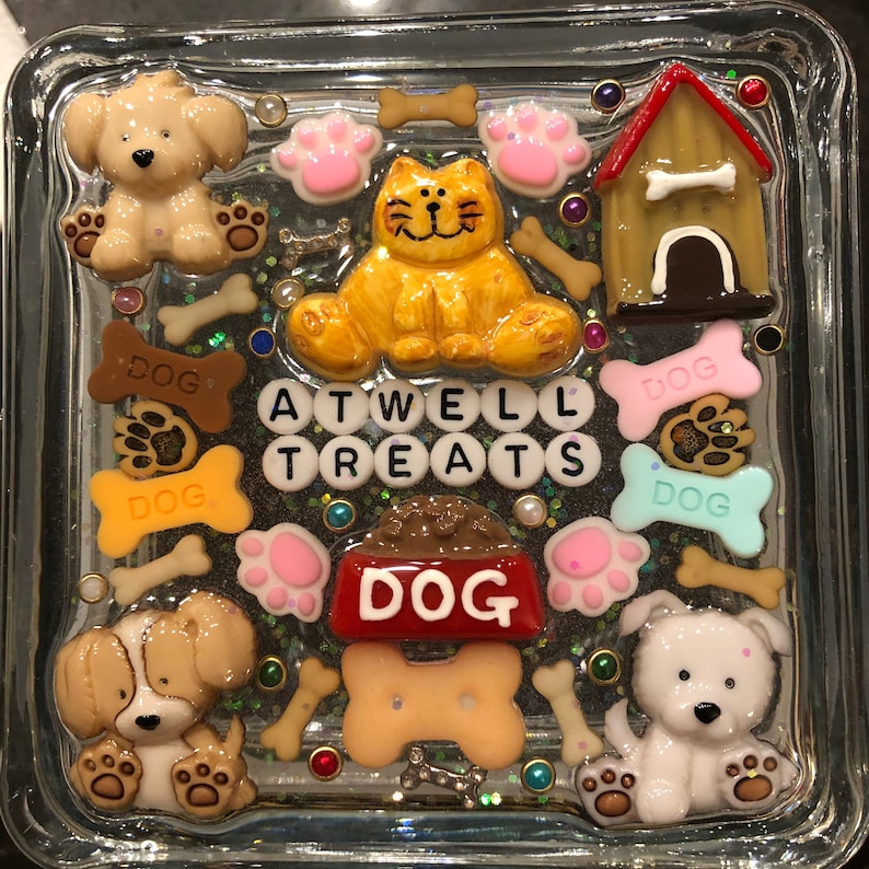 May include: A glass square box with a glittery background and various dog-themed decorations. The decorations include a dog house, dog bones, paw prints, and the words "ATWELL TREATS DOG".