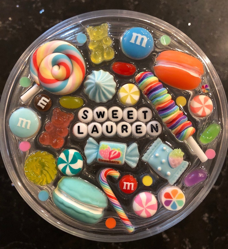 May include: A clear round resin tray with a variety of colorful candy and sweets, including lollipops, gummy bears, macarons, and candy canes. The tray also features the name "SWEET LAUREN" spelled out in white letters.