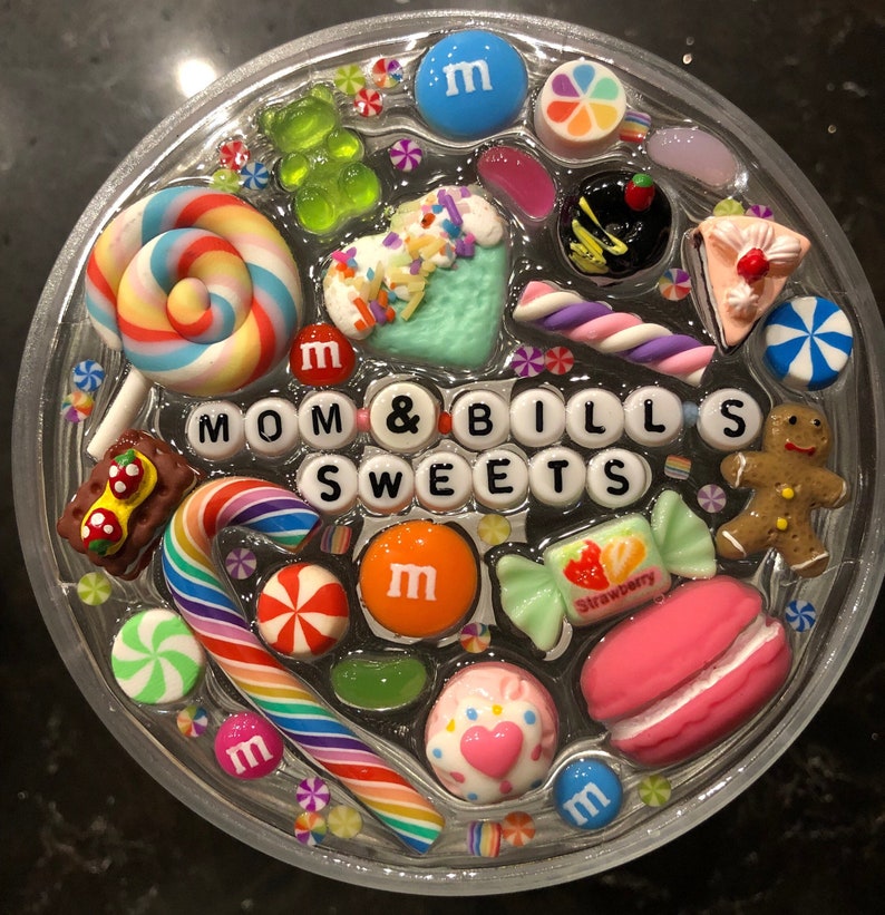 May include: A clear round tray filled with colorful candies, lollipops, and other sweets. The tray has the words "MOM & BILL'S SWEETS" spelled out in white letters.