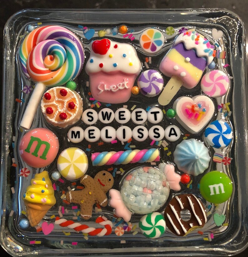 May include: A clear glass square with a colorful resin design featuring candy, sweets, and the name "Sweet Melissa".