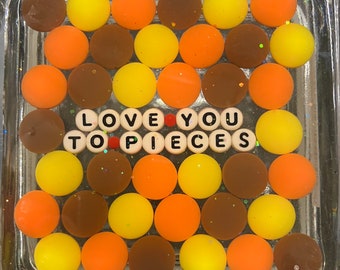 May include: A square glass tray filled with colorful round candies, spelling out the phrase "LOVE YOU TO PIECES" in white letter tiles.