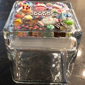 May include: A clear glass jar with a lid decorated with colorful candy and sprinkles. The lid has the words "Sweet Melissa" written on it.