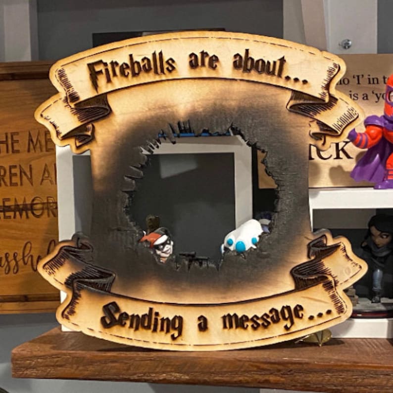 May include: A wooden sign with a burnt-out centre, shaped like a frame. The sign has a banner at the top that reads "Fireballs are about..." and another banner at the bottom that reads "Sending a message..."