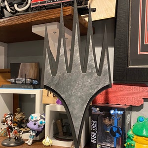 May include: A black and silver metal wall decor in the shape of a five-pointed star. The star is mounted on a wooden shelf with other decorative items, including a toy train, a small figurine, and a pop culture figure.