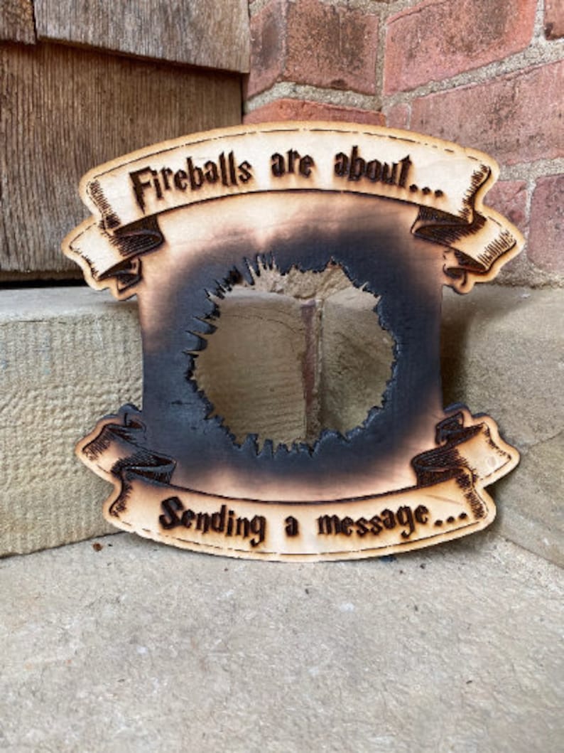 May include: A wooden sign with a burnt-out centre, featuring the text "Fireballs are about... Sending a message..." in a decorative font.