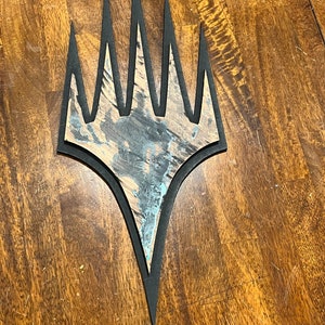 May include: A black and white wooden cutout of the Magic: The Gathering symbol, a five-pointed star with a jagged edge.