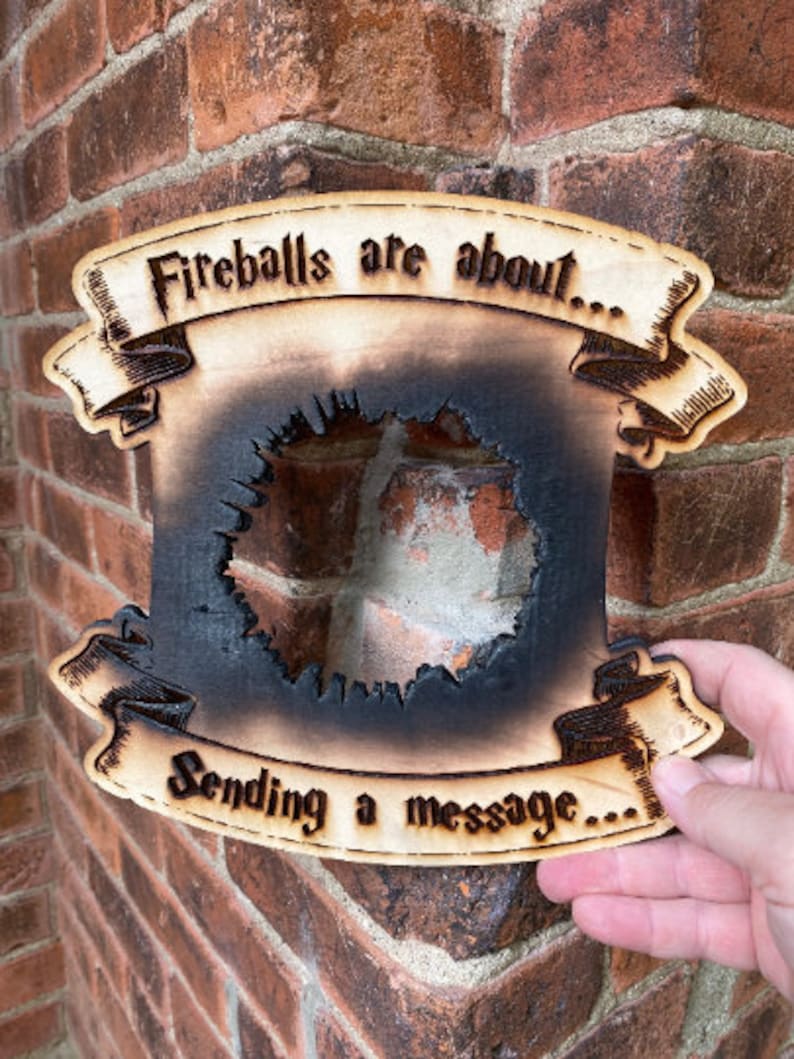 May include: A wooden sign with a burnt-out centre, resembling a fireball. The sign reads "Fireballs are about... Sending a message..."