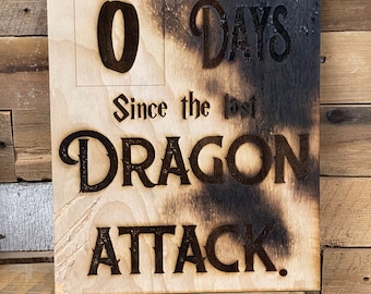 May include: A wooden sign with a burnt effect, displaying "0 DAYS Since the last DRAGON ATTACK."