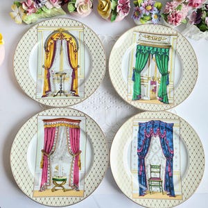 May include: Set of four decorative porcelain plates. Each plate features a central image of a window with ornate curtains in yellow, green, pink, and blue. The plates have a gold rim and a diamond pattern.