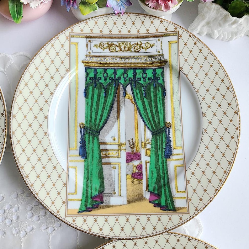 May include: A decorative plate with a cream-colored background and a gold diamond pattern around the rim. The center features a detailed illustration of a green curtained doorway with gold accents. The plate has a gold trim.