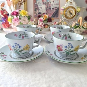 May include: Set of four white teacups and saucers with floral designs. The cups and saucers have a green trim and feature a variety of colorful flowers.