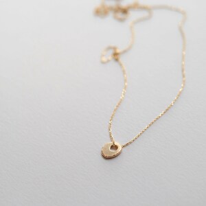 May include: A delicate gold chain necklace with a small, textured, heart-shaped pendant.