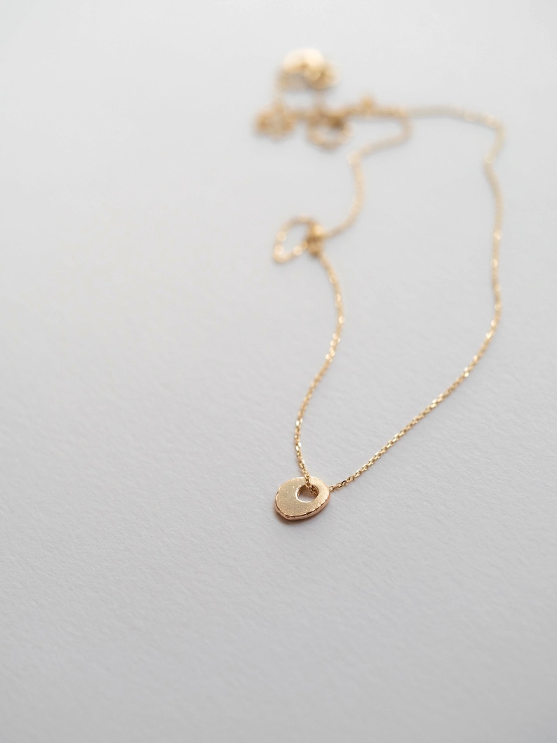 May include: A delicate gold chain necklace with a small, textured, heart-shaped pendant.