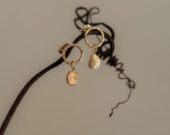 May include: Gold earrings with a hammered circle pendant hanging from a small gold hoop.