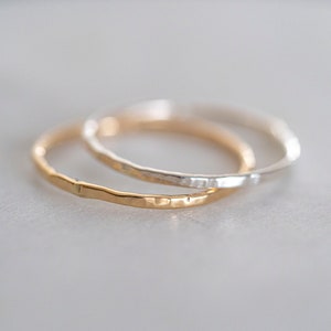 Puede incluir: Dos anillos finos de metal martillado, uno dorado y otro plateado, est&aacute;n apilados uno encima del otro.