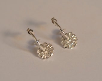 May include: A pair of silver hoop earrings with a flower design. The earrings are simple and elegant.
