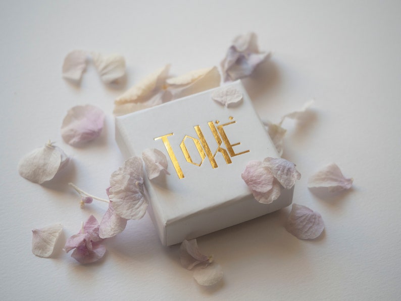 May include: A white box with the word "TOKE" printed in gold letters. The box is surrounded by pink and white flower petals.
