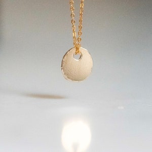 May include: A gold chain necklace with a round, textured pendant. The pendant has a small hole in the center.
