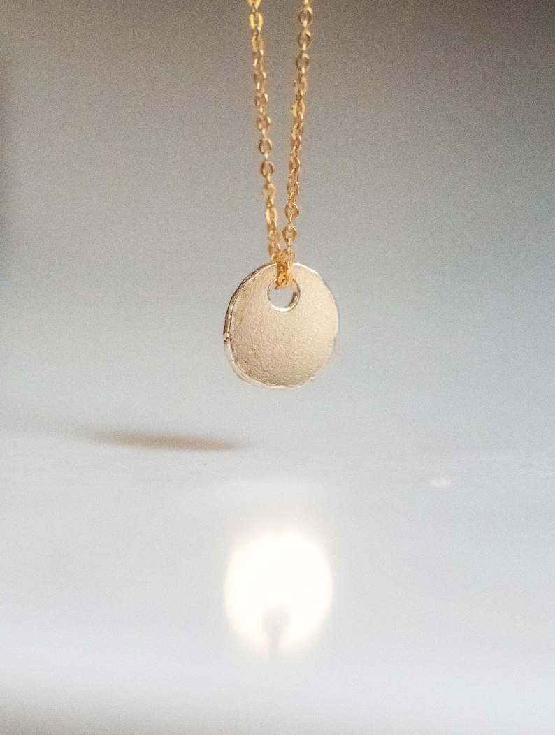 May include: A gold chain necklace with a round, textured pendant. The pendant has a small hole in the center.