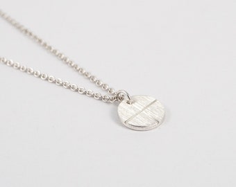 May include: A silver necklace with a small, round pendant featuring a textured, cross-shaped design.