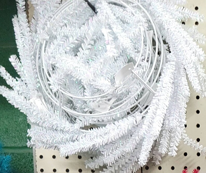 以下が含まれることがあります： ワイヤーフレームが付いた白くてふわふわのクリスマスリース。リースは白くて羽根のような枝で作られており、ホリデーシーズンに家を飾るのに最適です。