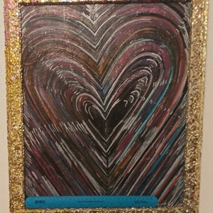 May include: A framed painting of a heart with a black background and colorful lines. The frame is gold with glitter.