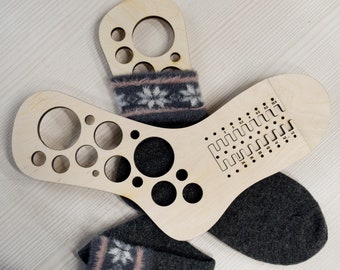 Könnte beinhalten: Zwei hölzerne Sockenspanner, einer mit einem Muster aus Kreisen und der andere mit einem Muster aus Linien und Punkten. Ein Paar graue Socken mit einem weißen und rosafarbenen Schneeflockenmuster liegt auf den Spannern.