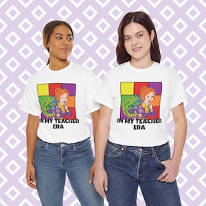 May include: Two people wearing white t-shirts with a colourful graphic of a woman with a lizard on her shoulder. The graphic has the text "In My Teacher Era".