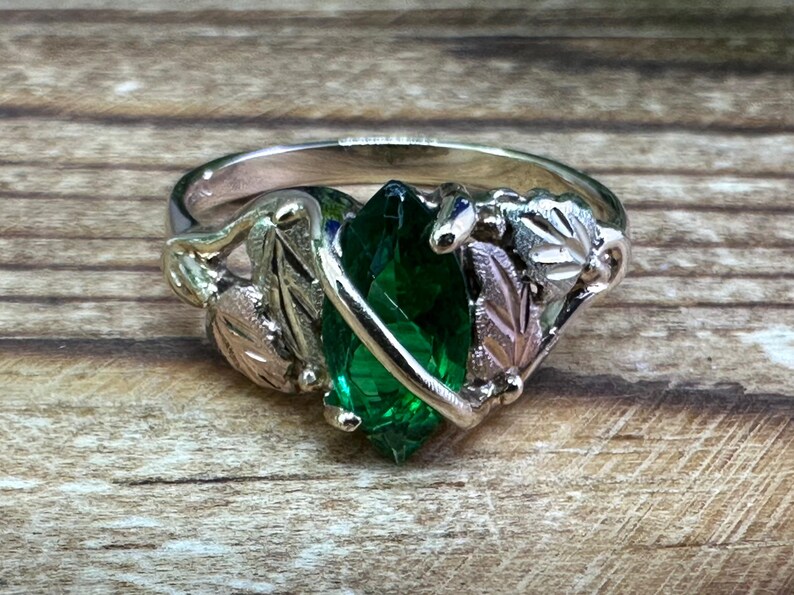 May include: A silver ring featuring a green gemstone set within gold and silver leaves.