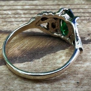 May include: A silver ring featuring a large green gemstone set in an intricate filigree design.