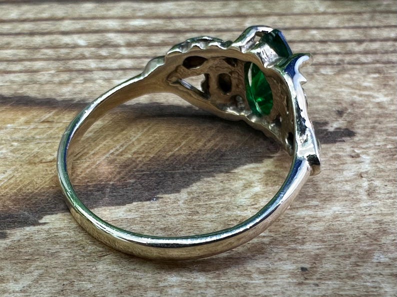 May include: A silver ring featuring a large green gemstone set in an intricate filigree design.