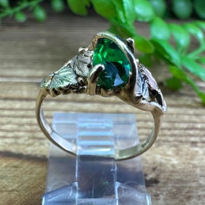 May include: A gold ring featuring a green gemstone set in a leaf design.