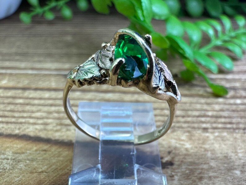 May include: A gold ring featuring a green gemstone set in a leaf design.