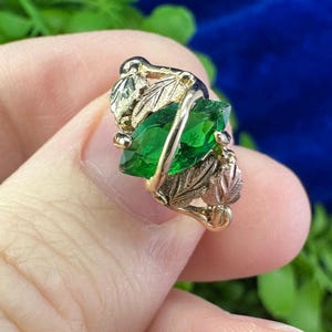May include: A gold ring with a green gemstone set in a leaf design.