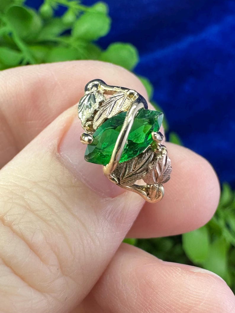 May include: A gold ring with a green gemstone set in a leaf design.
