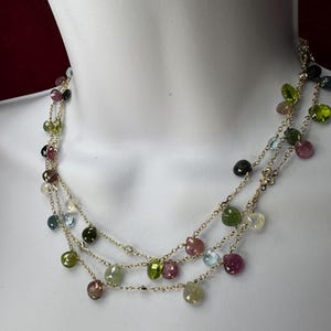 Peut inclure: Un collier multi-rangs avec une délicate chaîne dorée et des perles de pierres précieuses colorées. Les perles sont un mélange de pierres roses, vertes, bleues et transparentes.