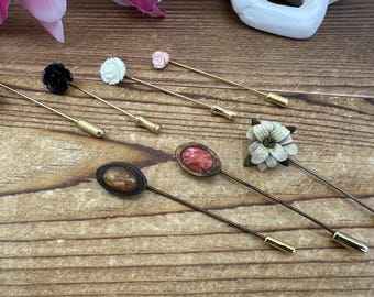 May include: A set of seven vintage gold tone hat pins with various flower and stone accents. The pins feature a white flower, a black flower, a pink flower, a white flower with a gold center, a red stone, a brown stone, and a white flower with a green center.