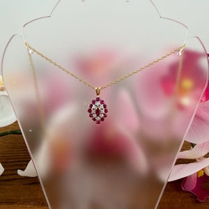 Op de afbeelding: Een gouden touwketting met een marquisevormige hanger. De hanger is bezet met een centrale robijn in marquiseslijpsel, omringd door een halo van kleine ronde witte diamanten en een buitenrand van ronde robijnen in een gouden zetting.
